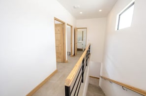 A narrow, well-lit hallway with wooden doors and a small window.