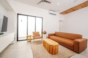A modern living room with a sofa, a coffee table, and a chair. There is a sliding glass door leading to a balcony.
