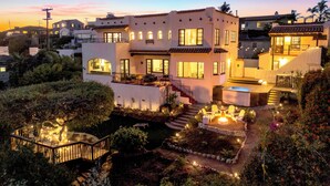 Uma casa moderna de dois andares com varanda, área de estar externa e um jardim bem iluminado.