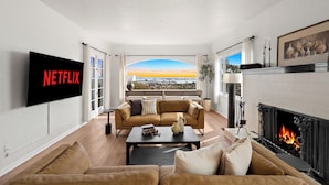 Uma sala de estar com uma televisão grande, lareira e vista para a cidade.
