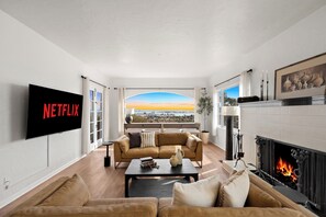A living room with a large TV, a fireplace, and a view of the city. - Spanish Manor by Coastline Vacation Rentals (San Diego)