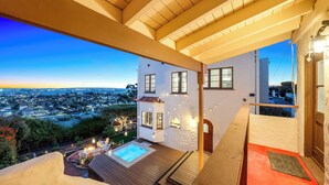 Varanda com vista para a paisagem urbana ao entardecer, uma banheira de hidromassagem e um espaço com carpete vermelho.