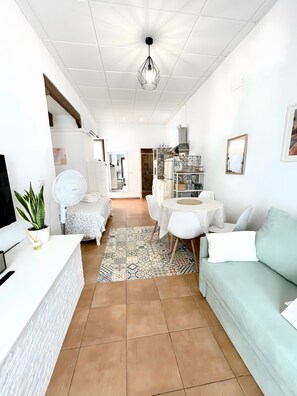 Ein modernes Wohnzimmer mit einer Couch, einem Esstisch und einer Küchenzeile inklusive Kühlschrank und Mikrowelle.
