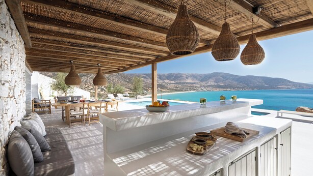 Une cuisine extérieure moderne avec vue sur la mer, une piscine et des montagnes en arrière-plan.