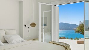 Une chambre avec un grand lit, une porte donnant sur un balcon avec vue sur la mer et les montagnes.