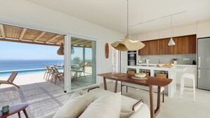 Une cuisine moderne avec vue sur l’océan, un coin repas avec une table et des chaises, et un espace salon confortable agrémenté de coussins.