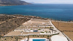 Vue aérienne d’une propriété située sur la côte, avec une piscine, des jardins aménagés et une route menant à la mer.