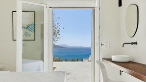 Une salle de bain moderne avec vue sur la mer, un lavabo blanc et une œuvre d’art encadrée au mur.