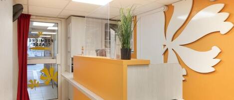 A reception area with a counter, a potted plant, and a decorative wall piece.