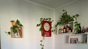 Ein Wohnzimmer mit einem orangefarbenen Sofa, einer roten Uhr und Regalen mit Pflanzen und Flaschen.