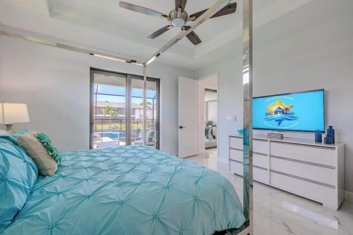 A bedroom with a bed, a ceiling fan, a television, and a sliding glass door leading to a balcony.