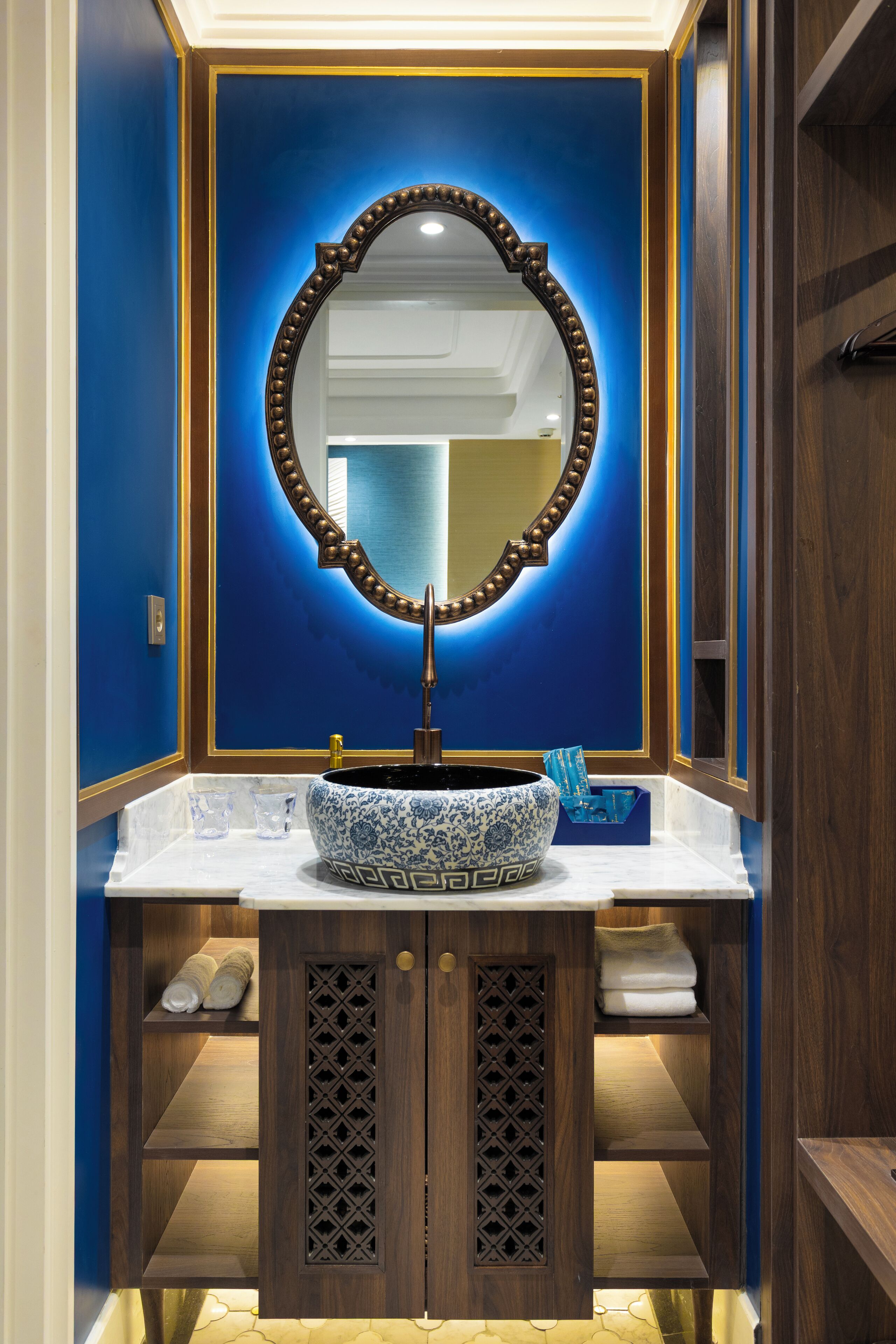Un baño con pared azul, tocador de madera, espejo grande y lavabo de cerámica azul y blanco.
