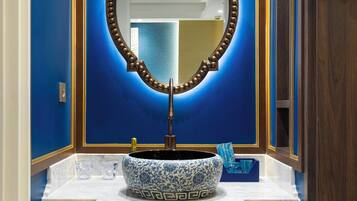Un baño con pared azul, tocador de madera, espejo grande y lavabo de cerámica azul y blanco.