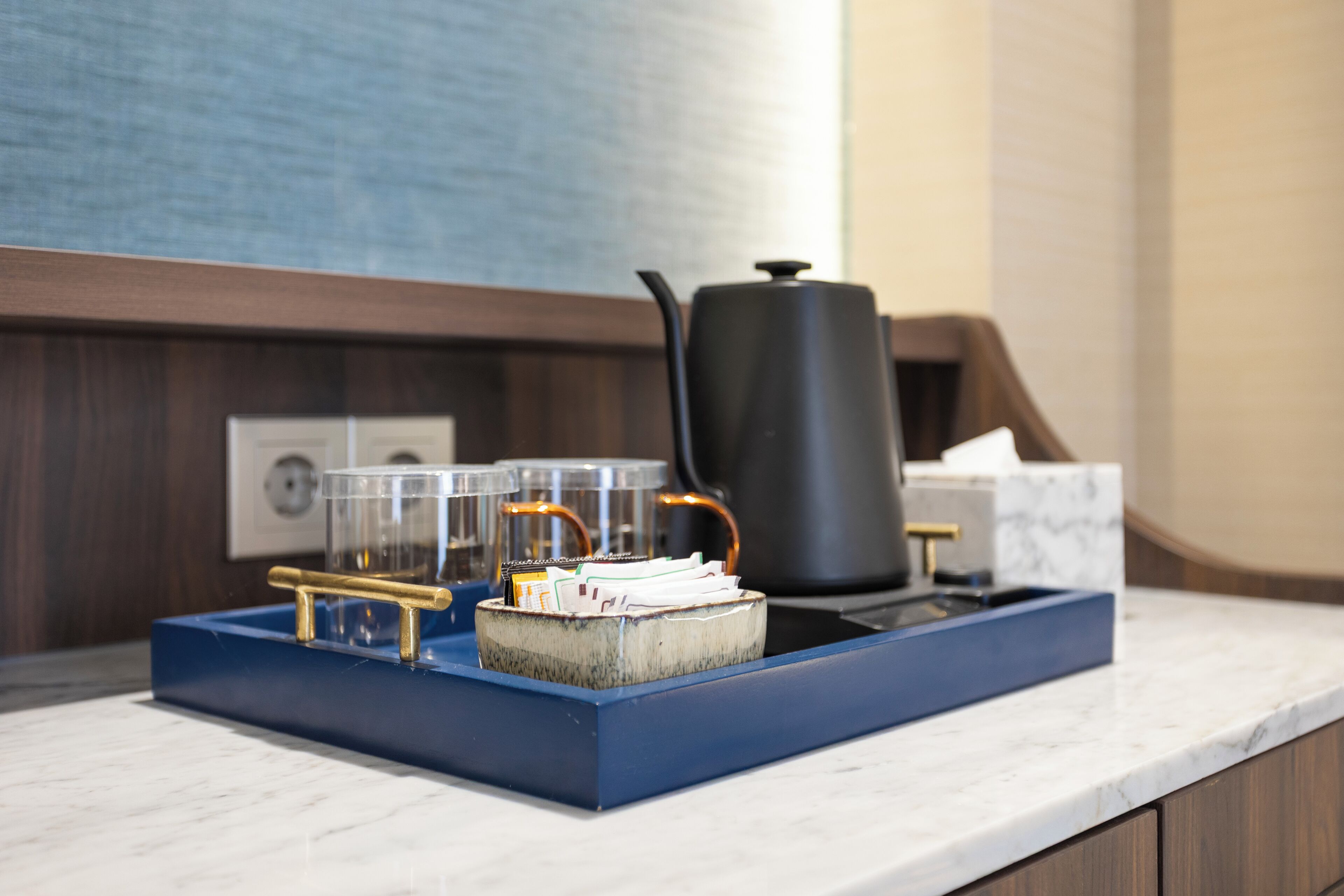 A kitchen counter with a blue tray holding a coffee pot, a kettle, and a stack of papers.
