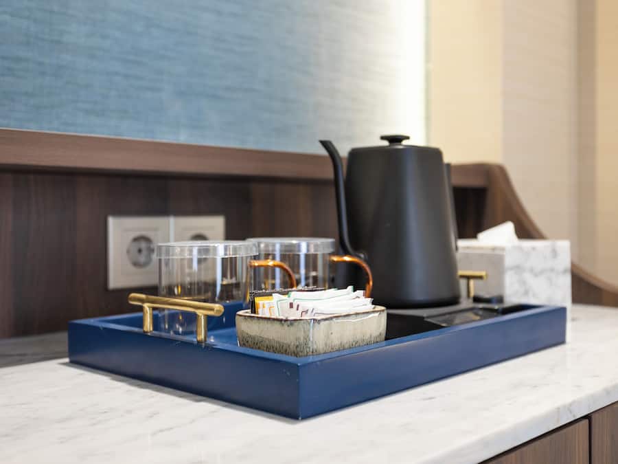 A kitchen counter with a blue tray holding a coffee pot, a kettle, and a stack of papers.