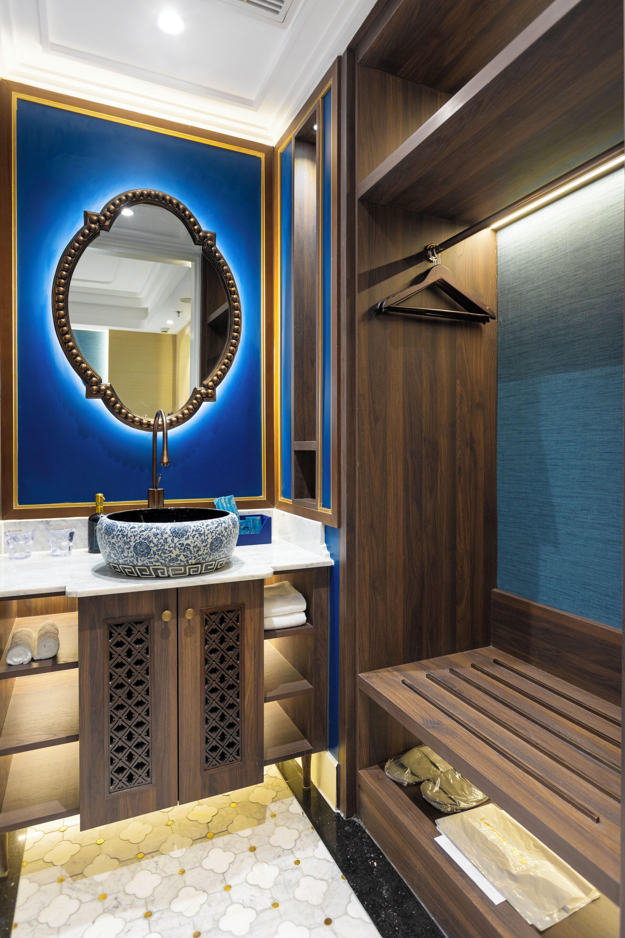 A bathroom with a large mirror, a vessel sink, wooden cabinetry, and a bench.