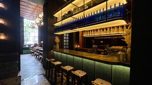 Una zona de bar con una barra alta, varias estanterías llenas de botellas y taburetes.