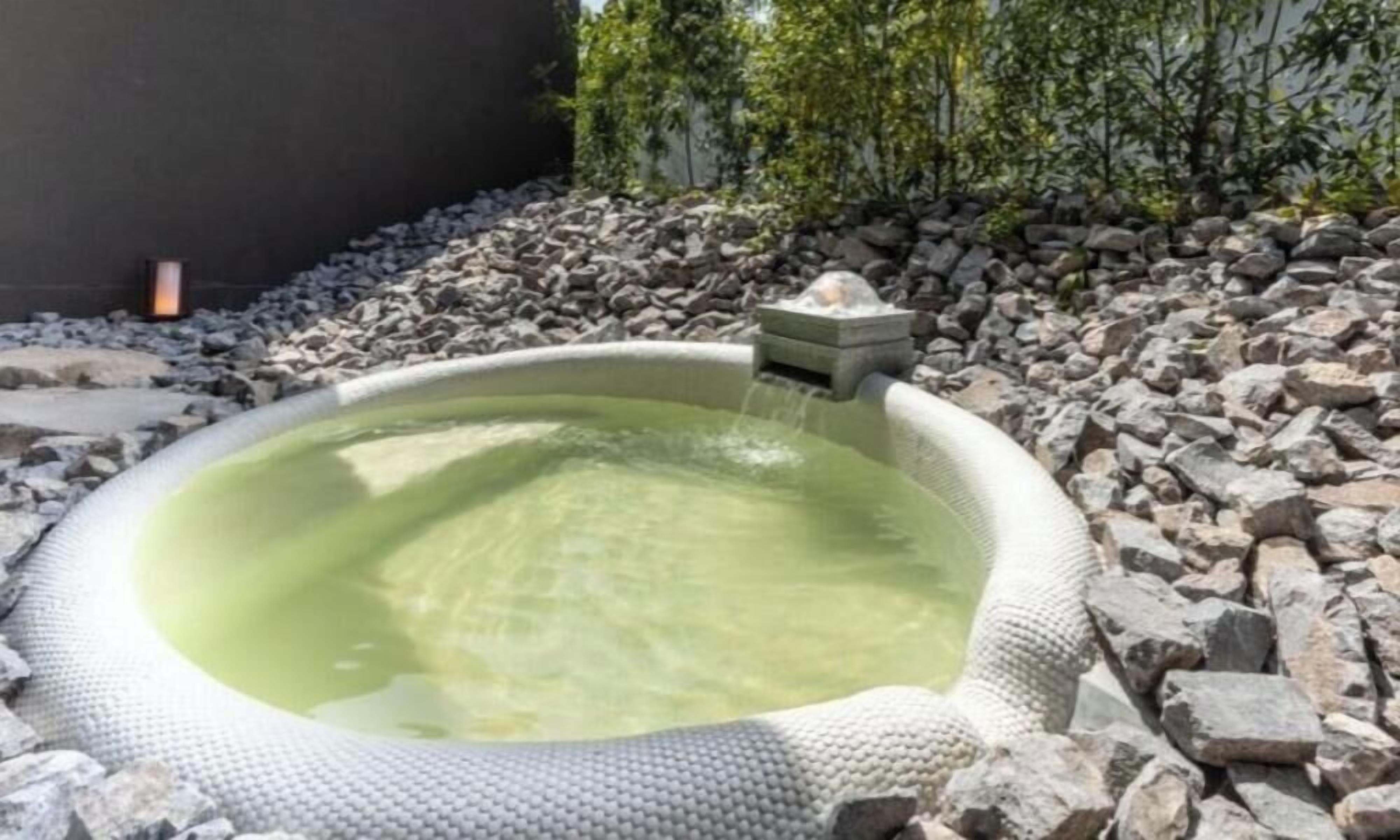 A hot tub with a stone surround, a stone pedestal, and a small waterfall feature.