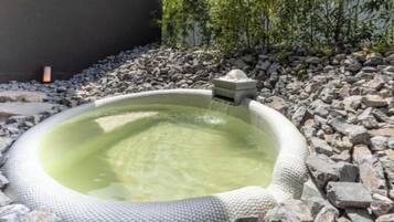 A hot tub with a stone surround, a stone pedestal, and a small waterfall feature.