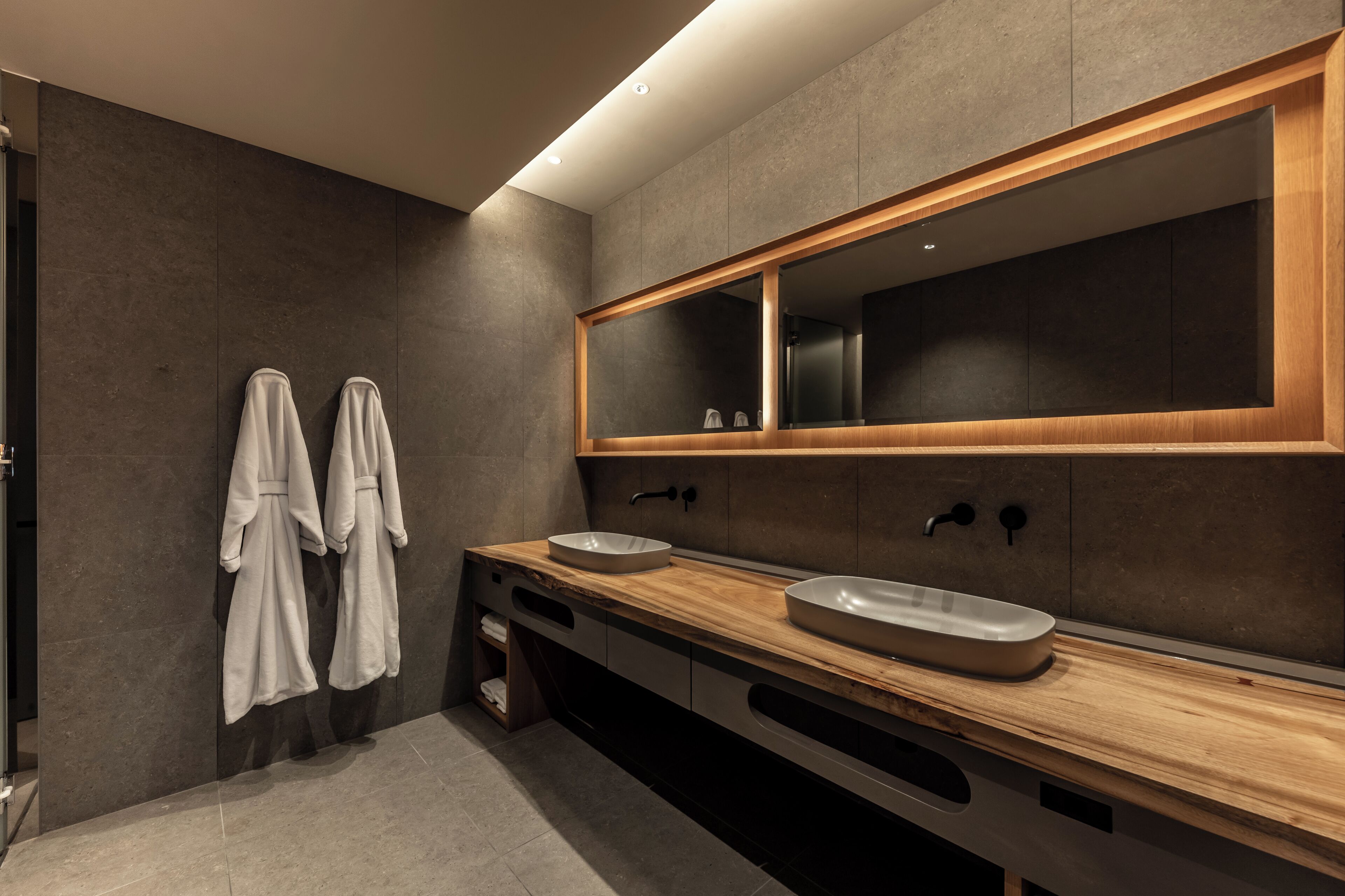 A modern bathroom with two sinks, a large mirror, and towels hanging on the wall.