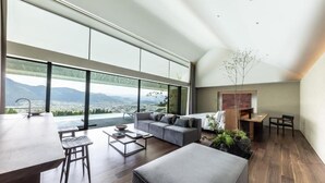 A spacious living area with a large window overlooking a mountainous landscape, a modern sofa, a coffee table, and a dining area with a wooden table and chairs. - ENOWA YUFUIN (Yufu)