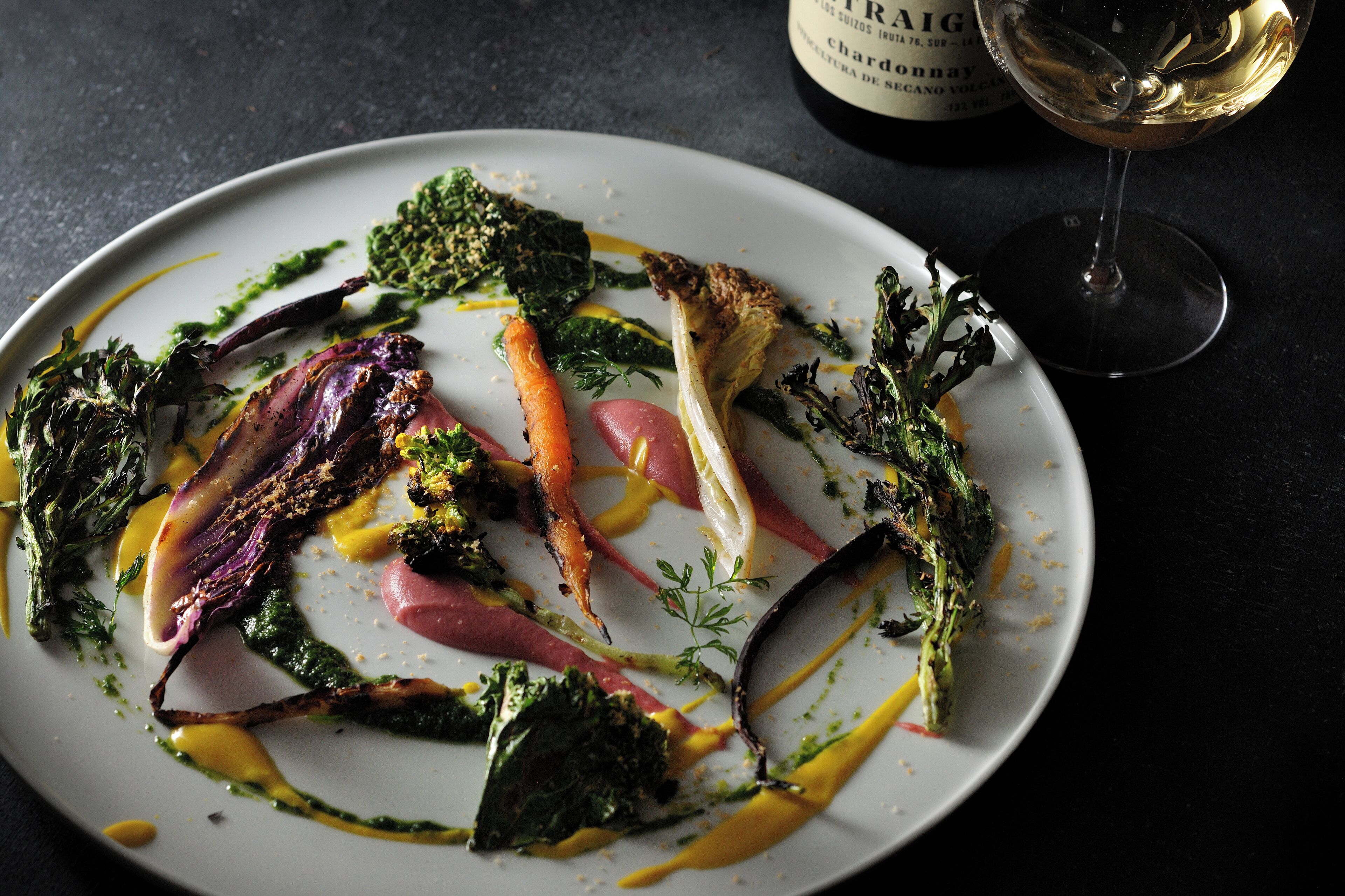 A plate of food with various vegetables and a glass of white wine.
