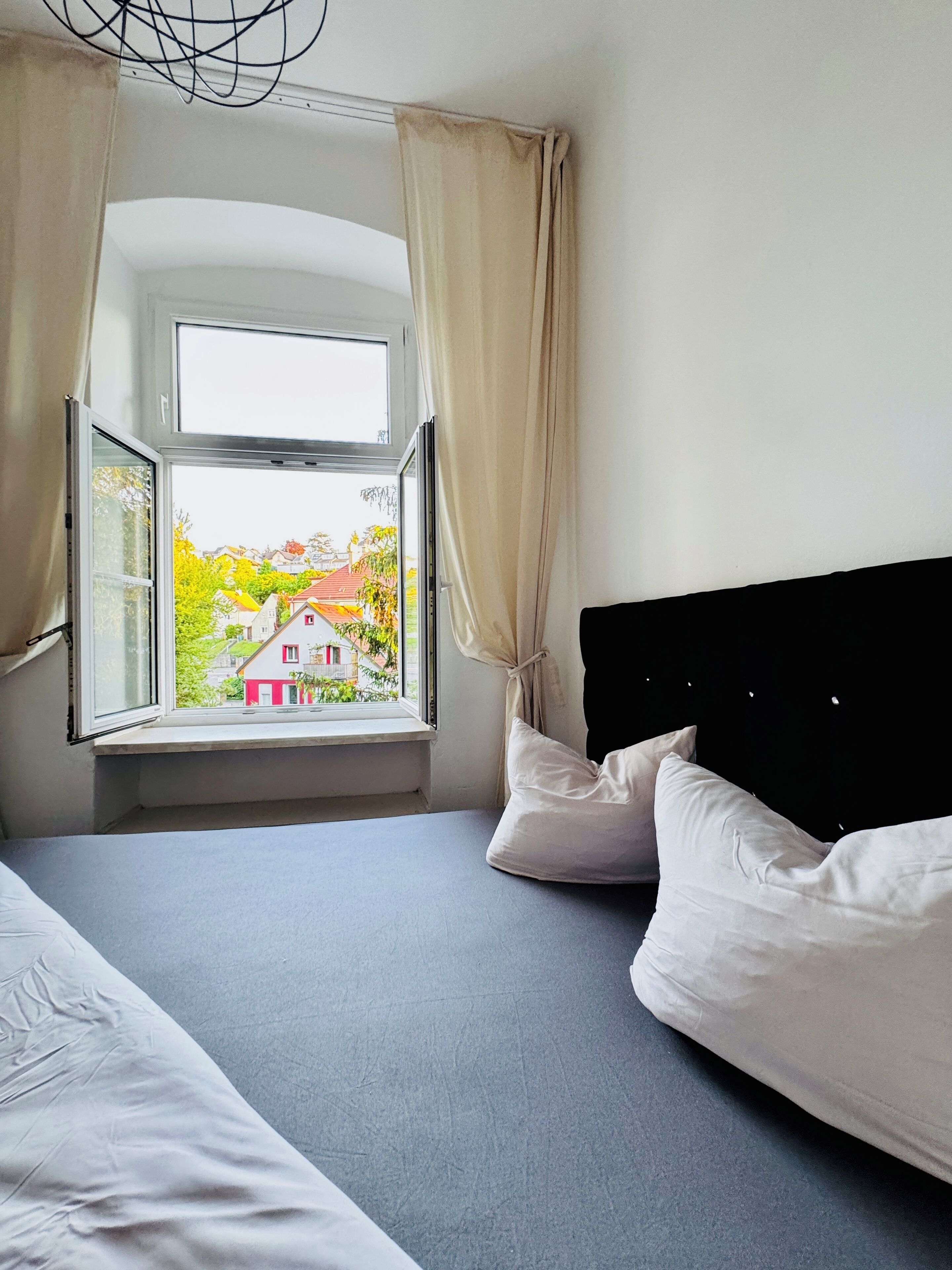 A bedroom with a large window, a bed, and a view of a red house and trees.
