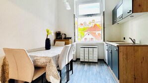 Une cuisine moderne avec un coin repas, comprenant une table avec des chaises, une machine à café et une vue sur une maison par la fenêtre.