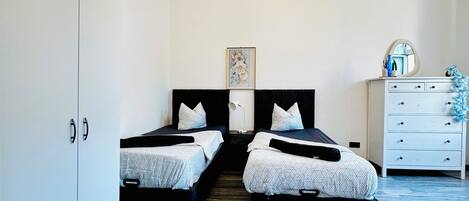 A bedroom with two beds, a dresser, a chandelier, and a framed picture on the wall.