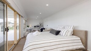 Ein modernes Schlafzimmer mit einem großen Bett, einem Schreibtisch und Blick durch eine Glastür.