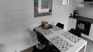 A modern kitchen with white cabinets, a microwave, and a coffee maker. There is a dining table with black chairs and a framed picture on the wall. - In the land of the Lapps Villa Pakatti (Kittilä)