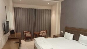Una habitación de hotel con cama, escritorio, silla, televisor y cortina.