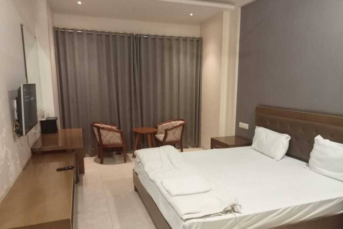Une chambre d’hôtel avec un lit, un bureau, une chaise, une télévision et un rideau.