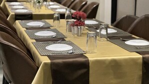 Un salón de conferencias con una larga mesa dispuesta para una reunión, equipado con tarjetas de identificación, platos, cubiertos y cristalería.