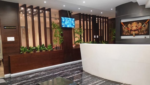 Una moderna zona de recepción de hotel con un mostrador de madera, una pantalla de televisión y una obra de arte enmarcada en la pared.