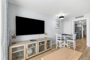 Ein modernes Wohnzimmer mit Flachbildfernseher, einer Holzkabine mit Glastüren, weißen Stühlen und einem Esstisch.