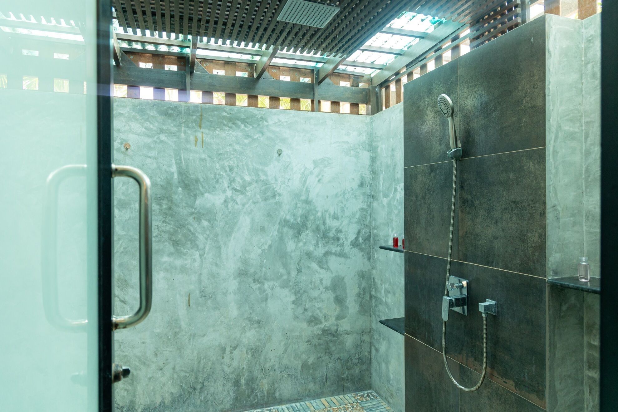 A modern shower area with a glass door, a metal handle, and a showerhead with a hose.