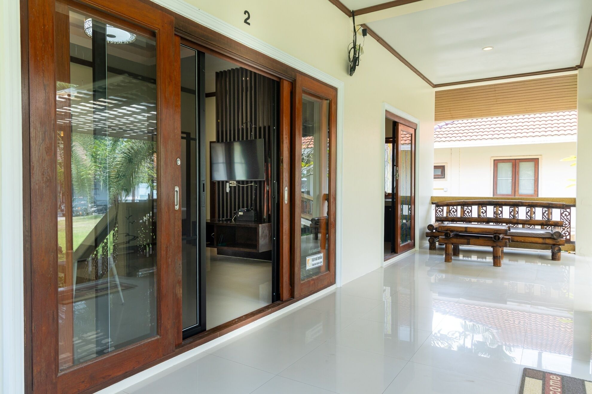 A hallway with a wooden bench, a large window with a view of greenery, and a door with a sign.