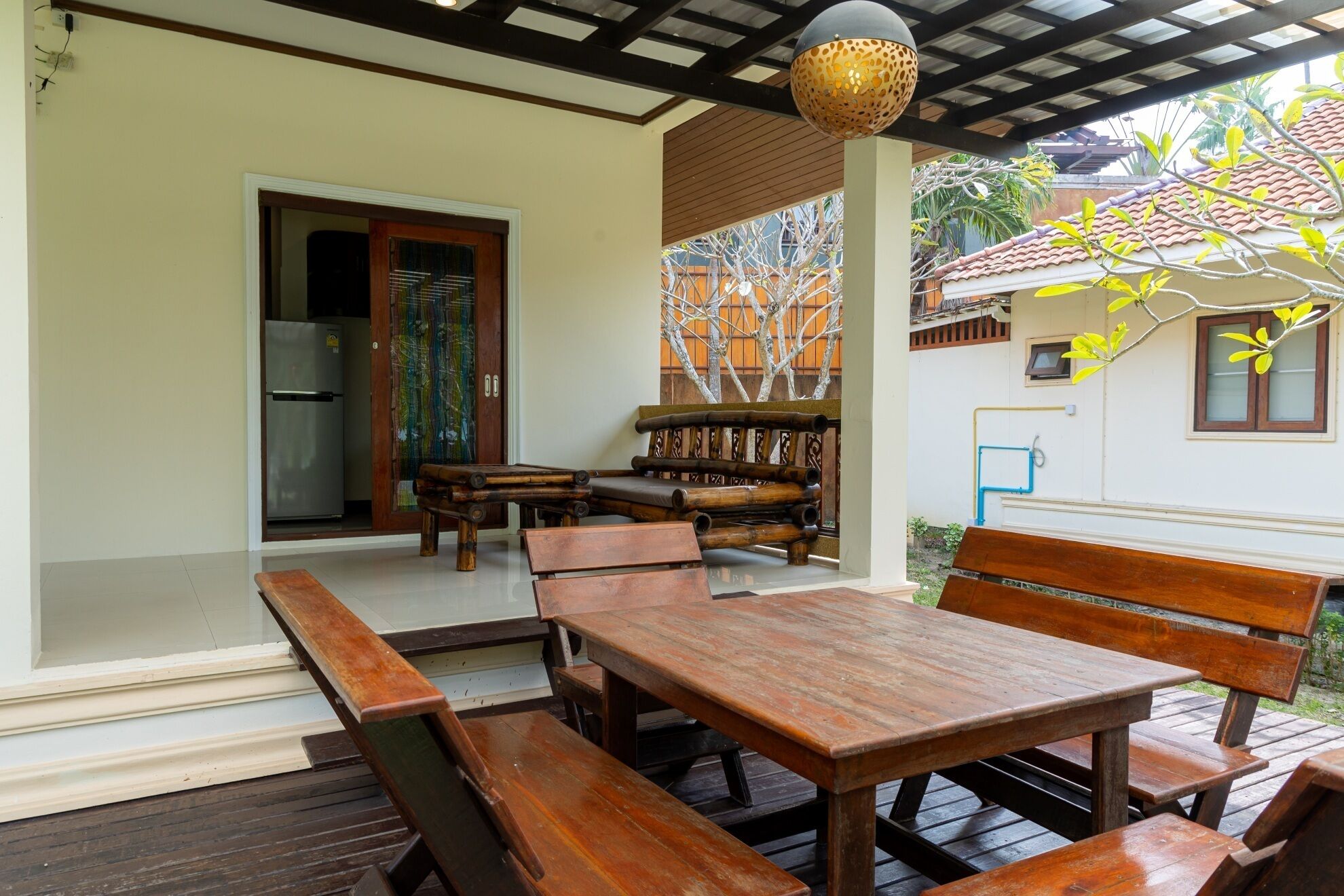 An outdoor patio with wooden tables and benches, a door leading inside, and a decorative wall with a tree mural.