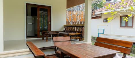 An outdoor patio with wooden tables and benches, a door leading inside, and a decorative wall with a tree mural.
