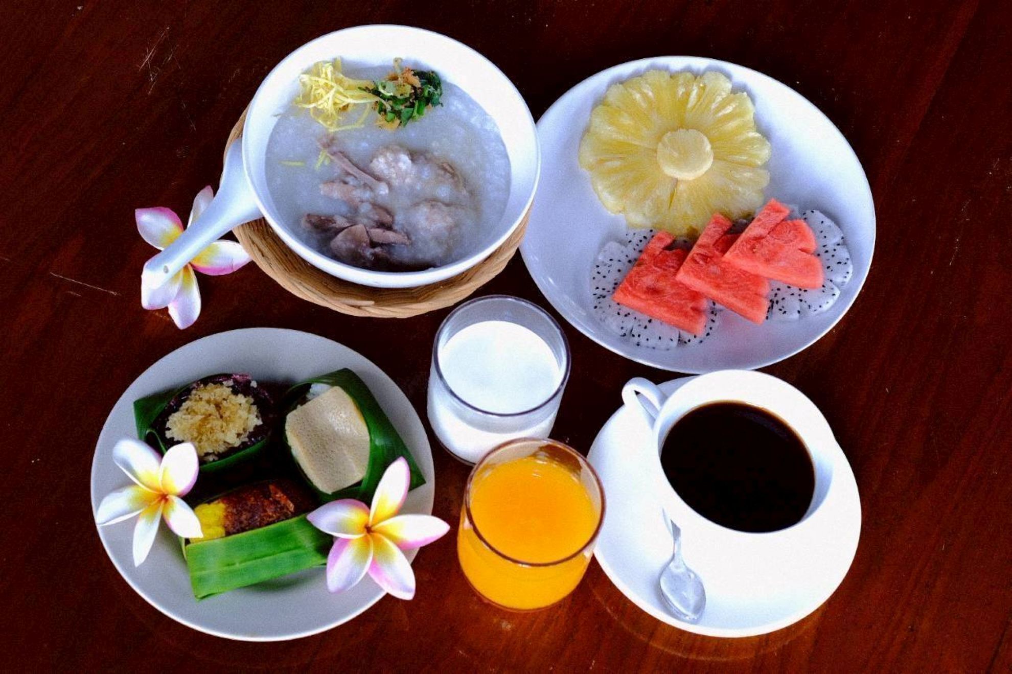 A table with a bowl of soup, a plate of fruit, a plate with a dessert, a glass of juice, and a cup of coffee.