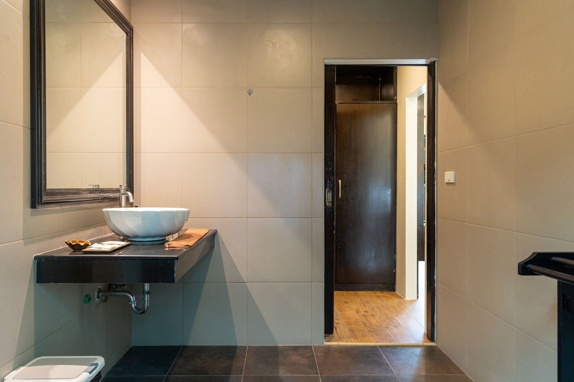 A modern bathroom with a large mirror, a white sink, and a dark floor.