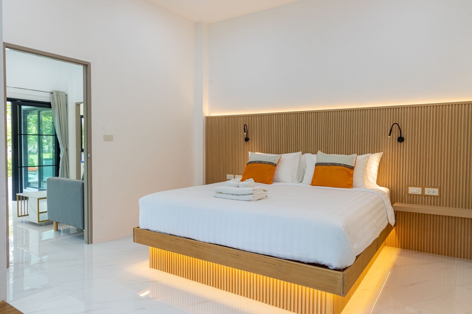 A modern bedroom with a large bed, wooden headboard, and a view of a balcony.