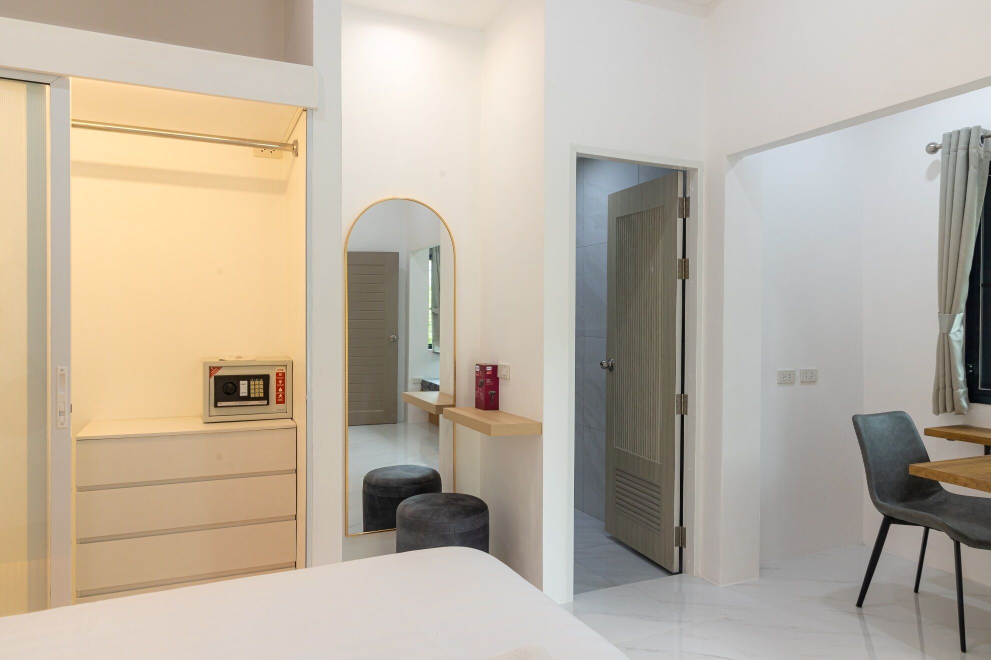 Ein modernes Hotelzimmer mit Bett, Schreibtisch, Stuhl, Spiegel und Kleiderschrank.