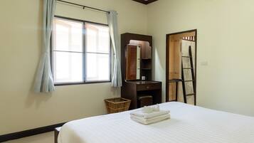 A hotel room with a bed, a wardrobe, a mirror, a window with curtains, a small wicker basket, and a ladder.