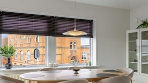 Een eetgedeelte met een ronde tafel, zes stoelen, een hanglamp, uitzicht op een bakstenen gebouw en een kast met glazen deuren.