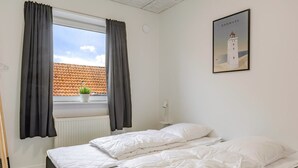 A bedroom with two beds, a window with curtains, a potted plant on the windowsill, and a framed picture of a lighthouse on the wall. - "Fader" - 31km from the sea by Interhome (Tønder)