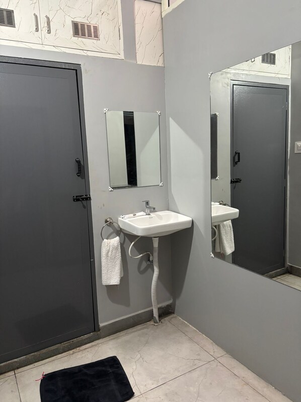 Un baño con una puerta gris, un lavamanos blanco, un espejo y un perchero para toallas.