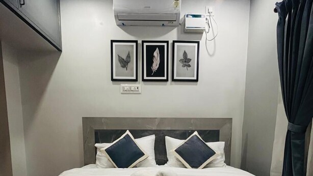 A neatly made bed with a heart-shaped towel arrangement, a wall-mounted air conditioner, and three framed leaf artworks. - KRS Paradise By  K Hotels  (Tiruvannamalai)