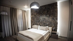 Moderni hotellihuone, jossa on suuri sänky, kivestä tehty koristeellinen seinä, yöpöytä ja lamppu.